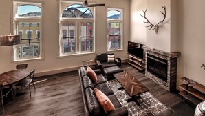 A spacious living room with a fireplace, leather sofas, a dining table, and large windows offering a view of buildings and hills. - The Salida Opera House Loft (Salida)