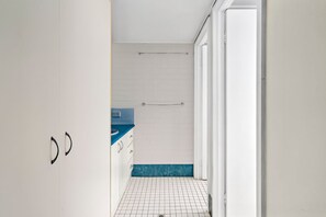 A narrow hallway with a white tiled floor, a blue accent wall, and a white door on the right. - Alinga U5 Kings Beach Apartment Ocean Views (KINGS BEACH)