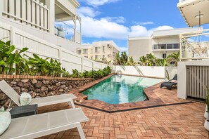 A swimming pool with a brick border, surrounded by lounge chairs and potted plants.