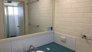 A bathroom with white tiled walls, a blue countertop, a sink, a mirror, and a shower area.