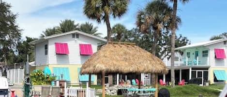 A waterfront property with a thatched-roof structure, palm trees, and colorful buildings with shutters.