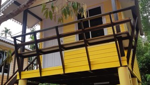 Een geel gebouw met een balkon, omringd door groen.