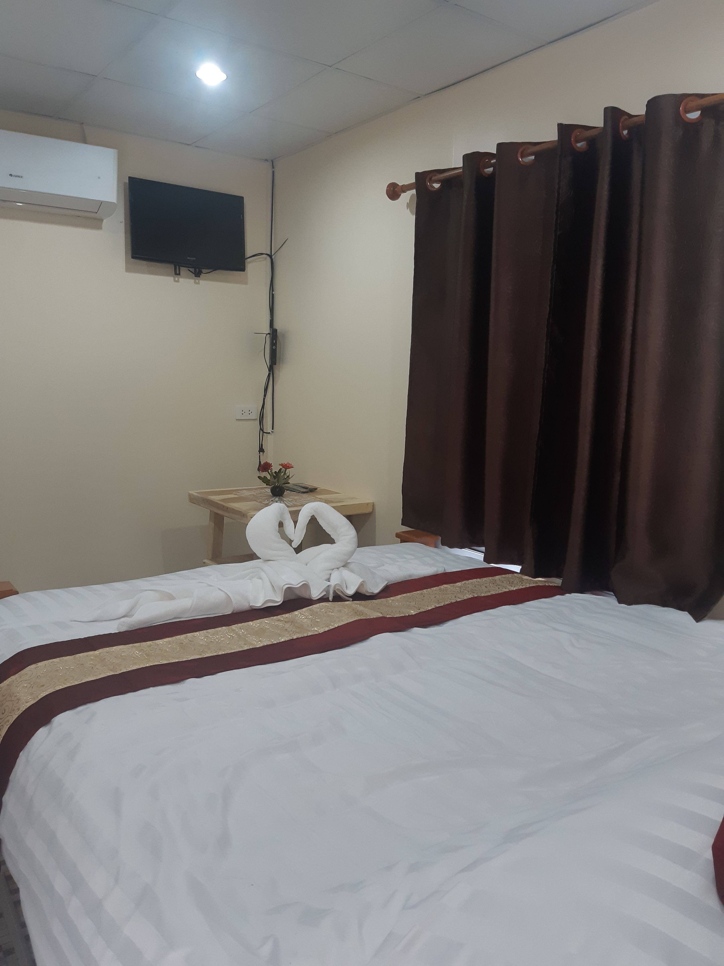 Camera d'albergo con un letto, una TV a schermo piatto montata a parete, un tavolino con un vaso di fiori e tende marroni.