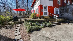 A red and white house with a stone pathway leading to the front door, surrounded by potted plants and a red umbrella. - Cleveland Home w/ South Saluda Fishing Access (Cleveland)