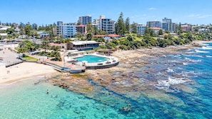 A coastal resort with a swimming pool, beachfront, and modern buildings in the background.