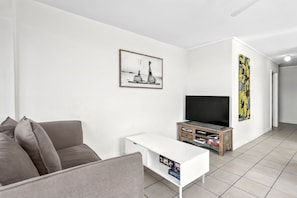 A modern living room with a grey sofa, a white coffee table, a wooden TV stand, and a framed picture on the wall.