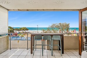 Un balcón con vista a la playa, dos sillas de metal y una mesa.