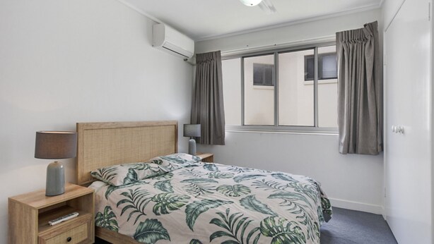 Une chambre à coucher comprenant un lit, deux lampes de chevet, une table de chevet, une fenêtre avec des rideaux et un appareil de climatisation.