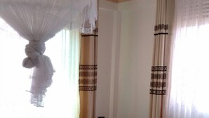 A neatly made bed with a white and brown bedspread, a wooden headboard, and a hanging white canopy. - United Motel Entebbe (Entebbe)