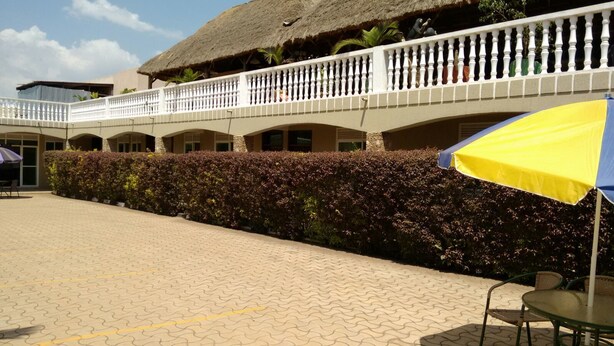 A hotel courtyard with a thatched-roof building, a white balustrade, and a hedge. - United Motel Entebbe (Entebbe)