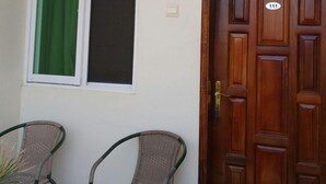 A room with a wooden door marked with the number 111, a window with a green curtain, and two wicker chairs. - United Motel Entebbe (Entebbe)
