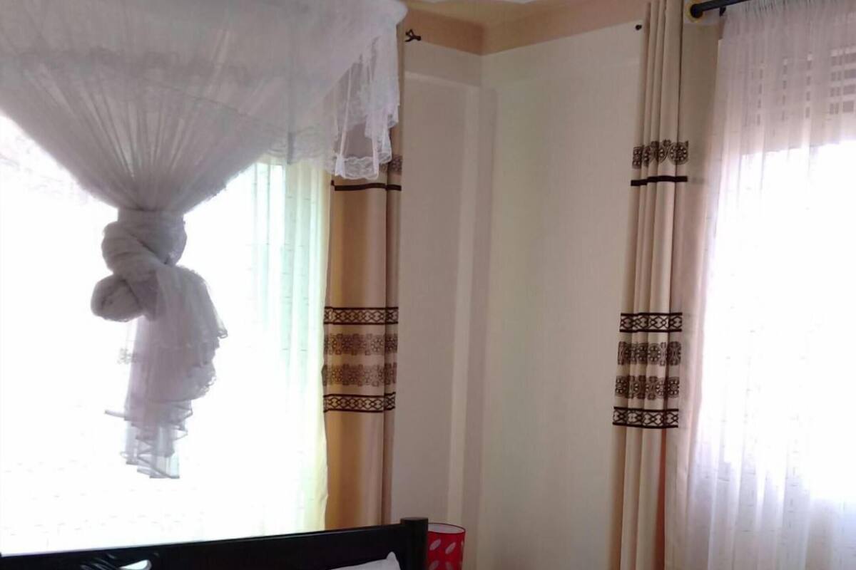 A neatly made bed with a headboard, a bedside table with a lamp, and curtains with a pattern.