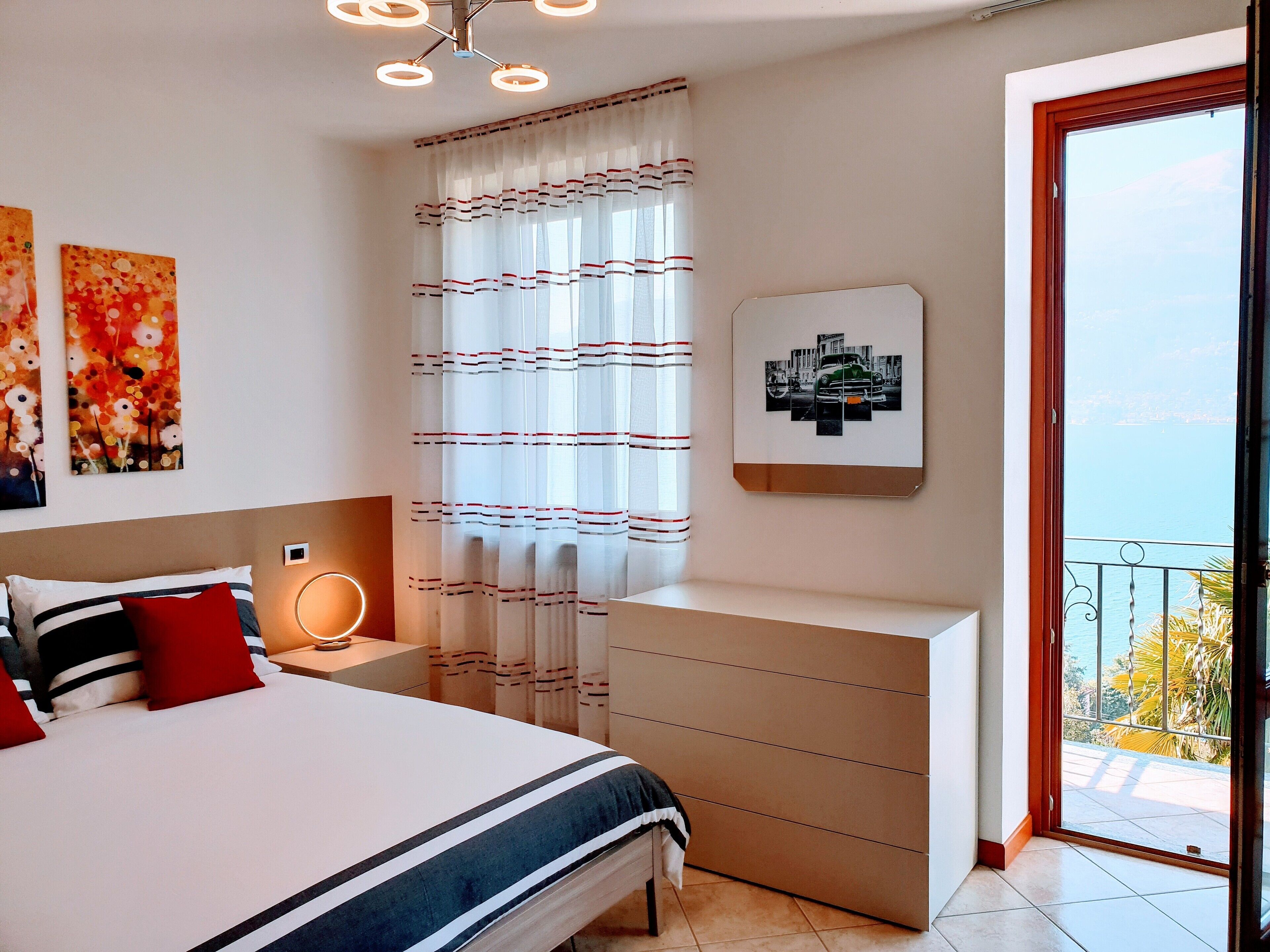 Een slaapkamer met een bed, nachtkastje en uitzicht op zee door een balkondeur.