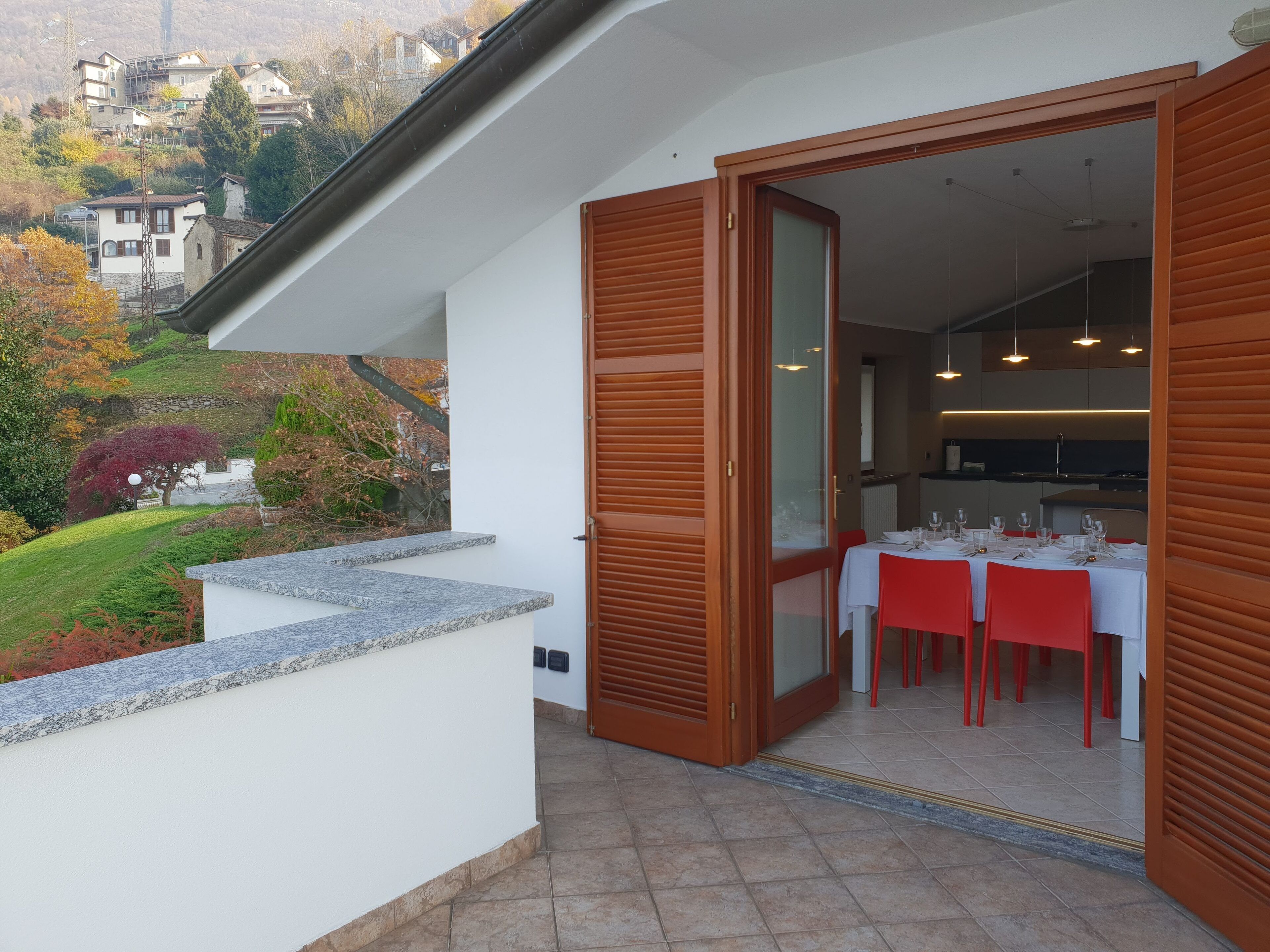 A dining area with a table set for four, a wooden door, and a view of a hillside with houses.