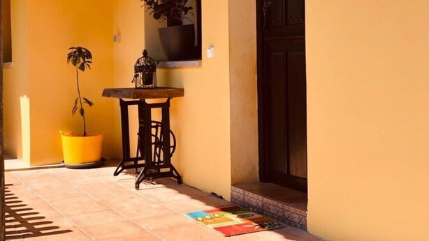 A sunlit hallway with a tiled floor, a potted plant, a table with a birdcage, and a door. - Holidays in Asturias (Asturias)