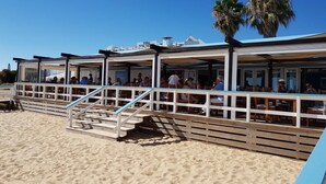 En restaurant ved stranden med udendørs siddepladser og en træterrasse.