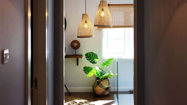 Un pasillo con una lámpara trenzada grande, una planta en maceta y piso de madera.