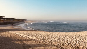 Una playa con cielo despejado, orilla de arena y algunas estructuras al fondo.