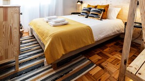 Un dormitorio con piso de madera, una cama con frazada amarilla, una mesita de noche, una lámpara y una cita enmarcada en la pared.