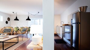 Una sala de estar moderna con comedor, piso de madera, cestos de mimbre y una cocina con refrigerador de acero inoxidable.
