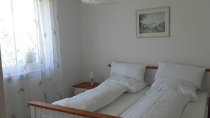 Une chambre à coucher avec un lit, une table de chevet, une lampe et une fenêtre avec des rideaux légers.