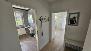 Un couloir menant à une salle de bain équipée d’un lavabo et d’une fenêtre, ainsi que d’un miroir fixé au mur.