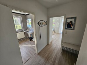 Ein Flur, der zu einem Badezimmer mit Waschbecken und Fenster führt, mit einem Spiegel an der Wand.