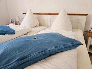 Ein Doppelbett mit Holz-Kopfteil, weißer Bettwäsche und einer blauen Tagesdecke.
