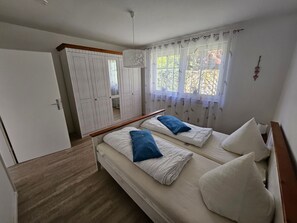 A bedroom with two beds, a wardrobe, and a window with curtains.