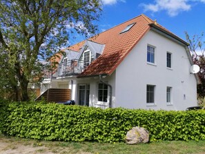 Une maison à deux étages, avec un toit à pente recouvert de tuiles rouges, des murs extérieurs blancs et une antenne parabolique.
