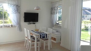 Un coin repas comprenant une table, des chaises, un téléviseur et une fenêtre avec des rideaux.