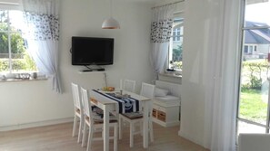 Ein Essbereich mit Tisch, Stühlen, einem Fernseher und einem fensterbepflanzten Fenster.