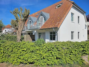A two-story house with a red-tiled roof, white exterior walls, and a balcony with a metal railing.