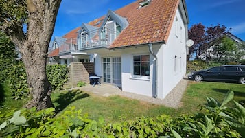 Ein zweistöckiges Haus mit rotem Ziegeldach, einem Balkon und einem kleinen Garten mit Grünpflanzen.