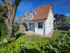 Ein zweistöckiges Haus mit rotem Ziegeldach, einem Balkon und einem kleinen Garten mit Grünpflanzen.
