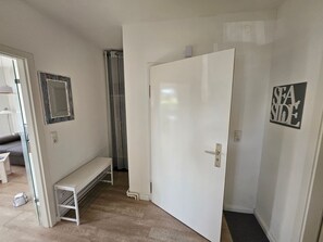 Ein Flur mit einer weißen Tür, einer Bank, einem Spiegel und einem Schild mit der Aufschrift 'SEA SIDE'.