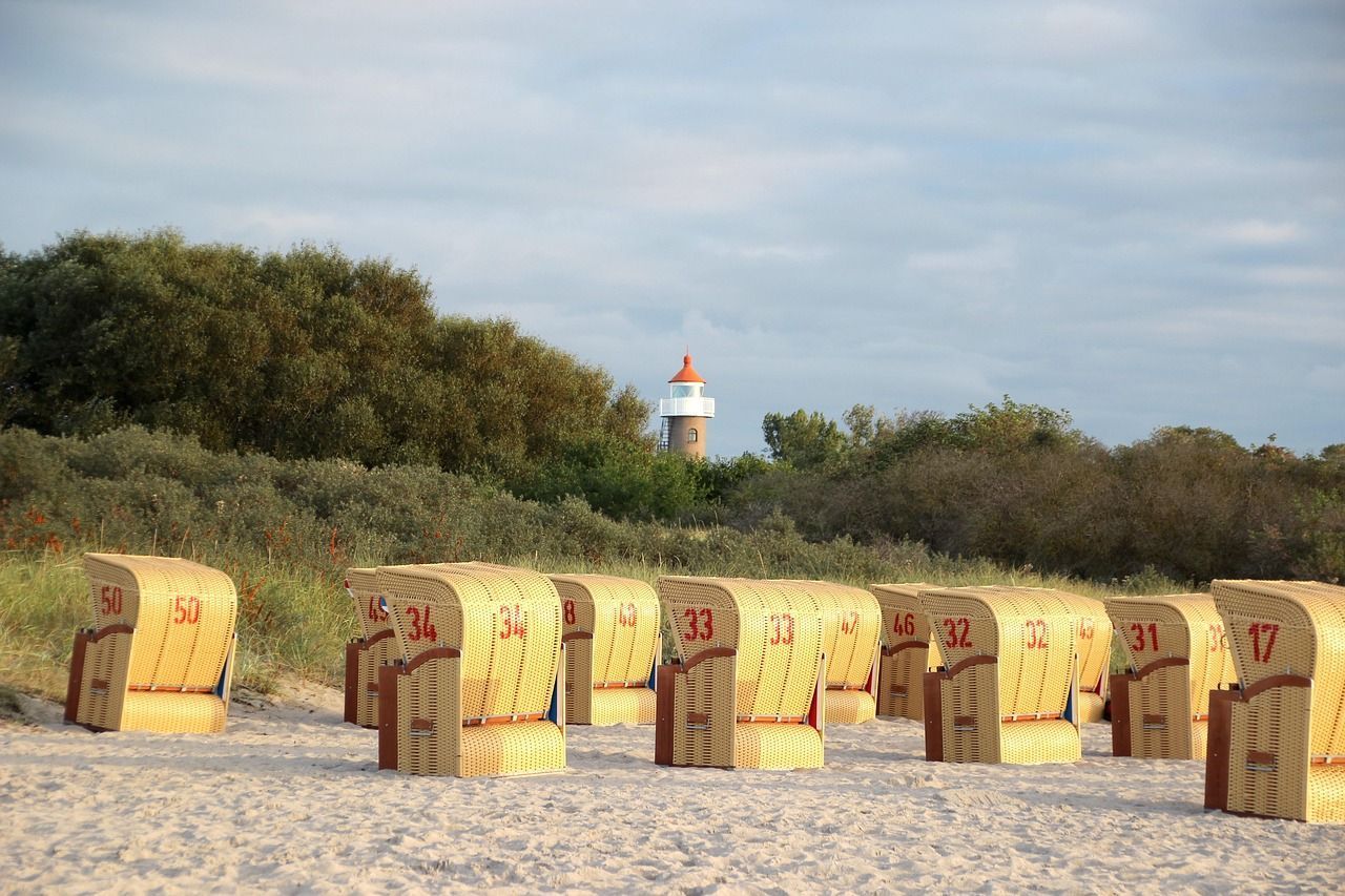Strandliegen mit den Nummern 17 bis 50 reihen sich an einem Sandstrand auf, im Hintergrund ist ein Leuchtturm zu sehen.