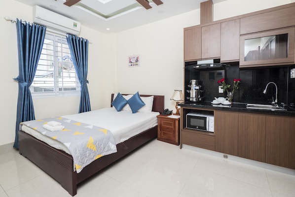 A bedroom with a bed, a nightstand, a built-in kitchen area, and a window with curtains. - Johnny Hotel (Da Nang)
