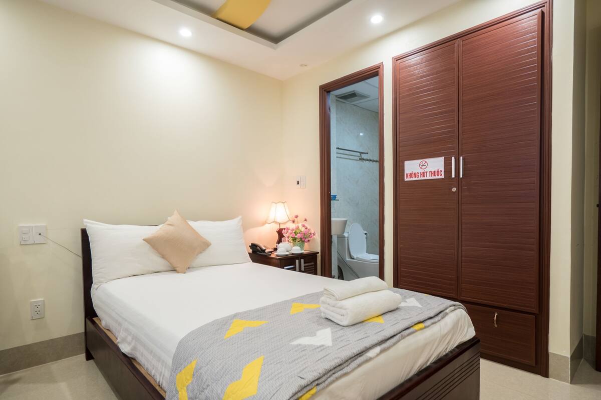 A hotel room with a bed, bedside table, lamp, and a wardrobe.
