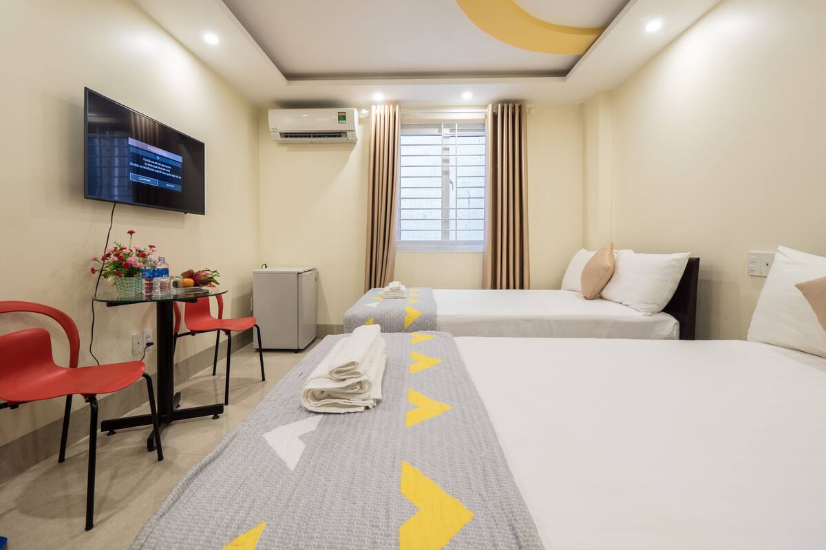 A hotel room with two beds, a desk with a chair, a TV, and a window with curtains.