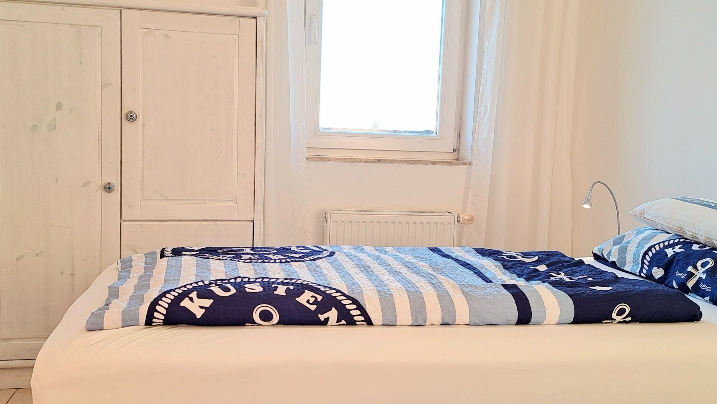 Un dormitorio con cama, ventana, radiador y armario.