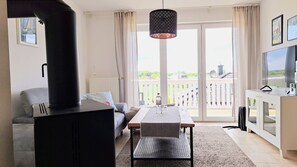 Un salon comprenant un canapé, une table, un téléviseur et une grande fenêtre donnant sur un balcon.