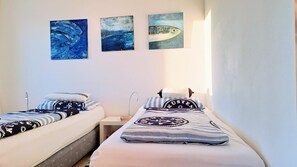 Ein Zimmer mit zwei Betten, jeweils mit Kissen und Decke, und drei Bildern an der Wand.