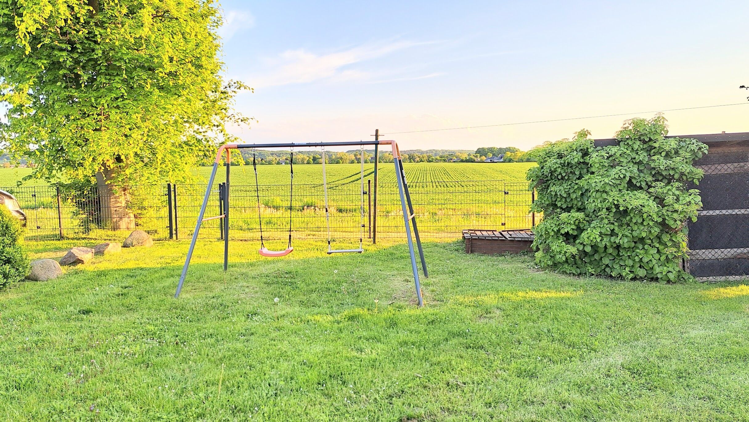 A grassy area with a swing set, a tree, and a fence.