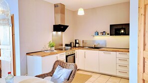 Une cuisine compacte avec des meubles blancs, un plan de travail en bois, un four encastré, une machine à café et un luminaire suspendu.