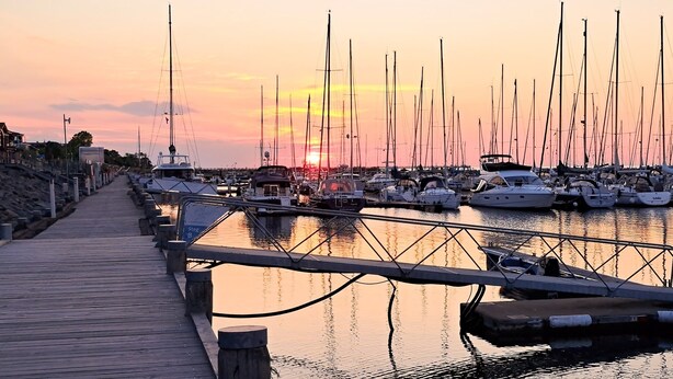 Un port de plaisance avec des bateaux amarrés, une promenade en bois et un coucher de soleil en arrière-plan.