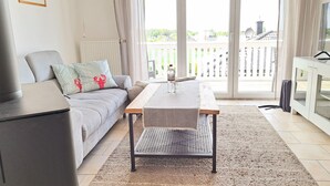 Un salon moderne avec un canapé, une table basse et une vue sur un balcon agrémenté d’une balustrade blanche.
