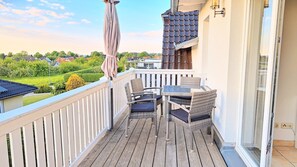 Ein Balkon mit Korbmöbeln, einem Glastisch und Blick auf die Nachbarschaft.