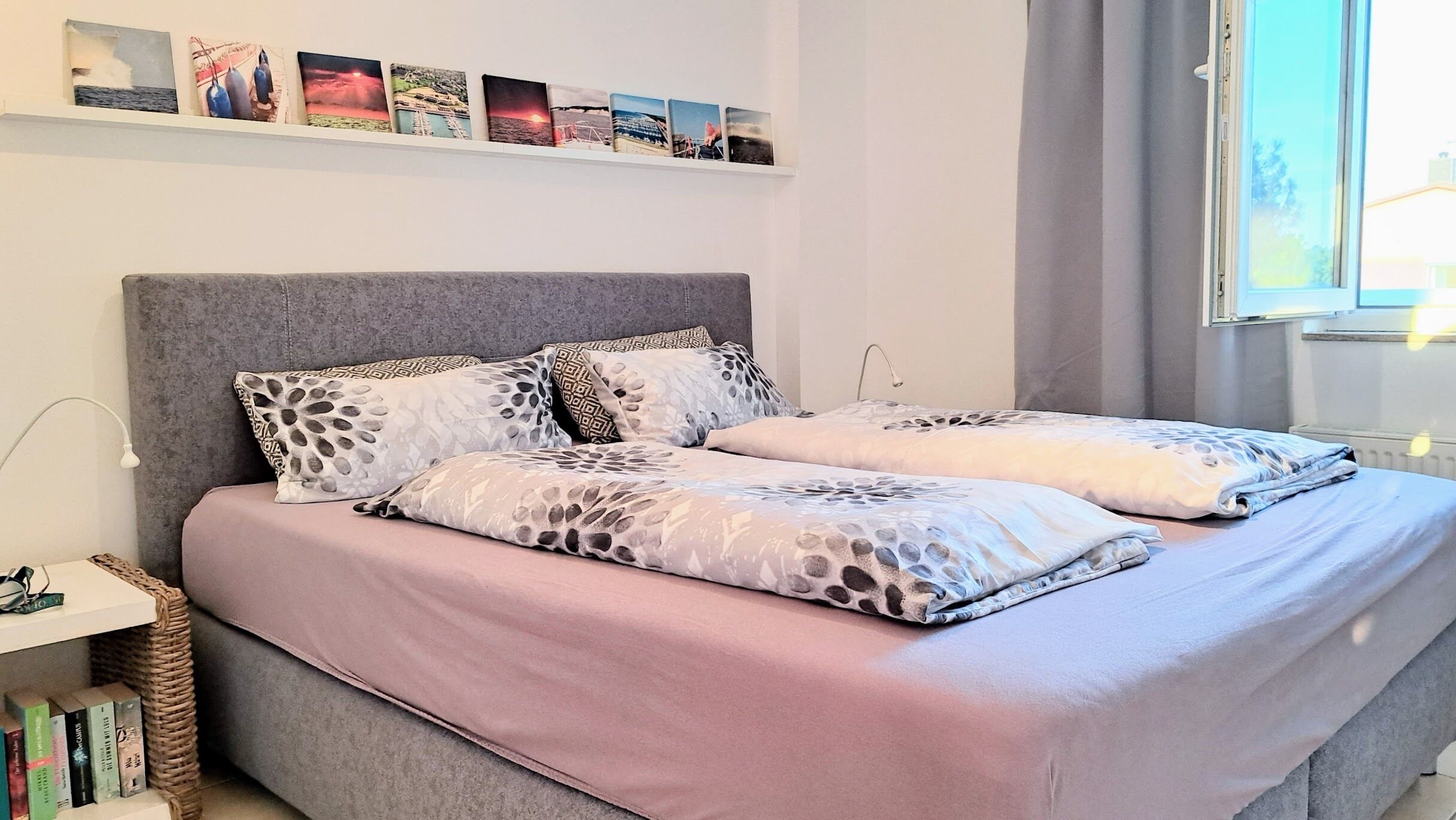 A bed with patterned bedding, a bedside table with books, and a wall with framed pictures.