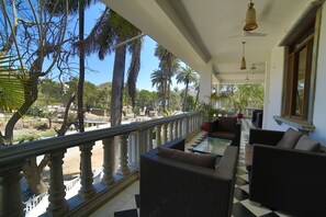 Un balcón con mobiliario de mimbre y vistas a palmeras y un paisaje distante.